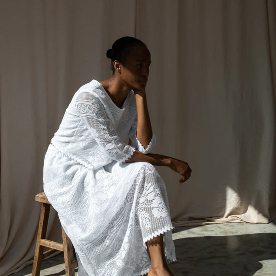 Woman in a white Beaumont organic co-ord sitting on a wooden stool against a plain background