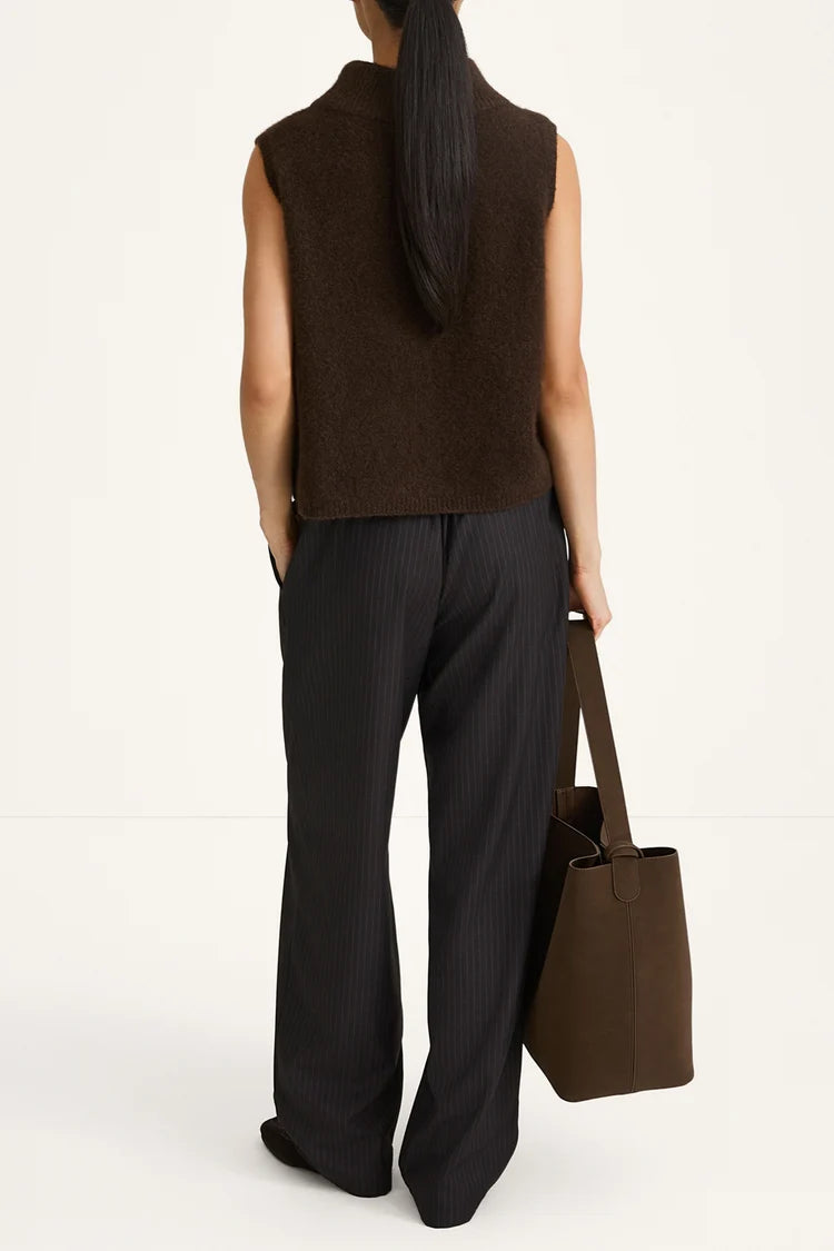 Person wearing a brown sleeveless top and black pants, holding a brown tote bag on a white background