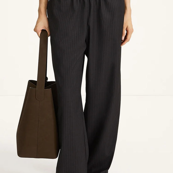 Person wearing black pants holding a brown bag on a white background