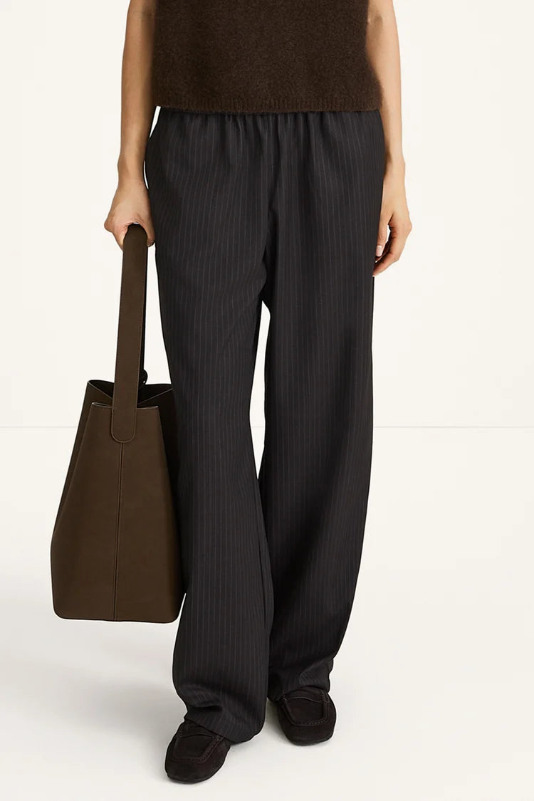 Person wearing black pants holding a brown bag on a white background