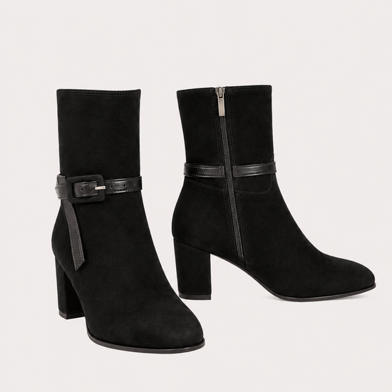 A pair of black suede ankle boots with block heels and a decorative strap detail across the ankle, shown against a light beige background.