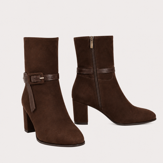 A pair of dark brown suede ankle boots with block heels and a matching faux-leather buckle strap around the ankle, shown against a plain light beige background.