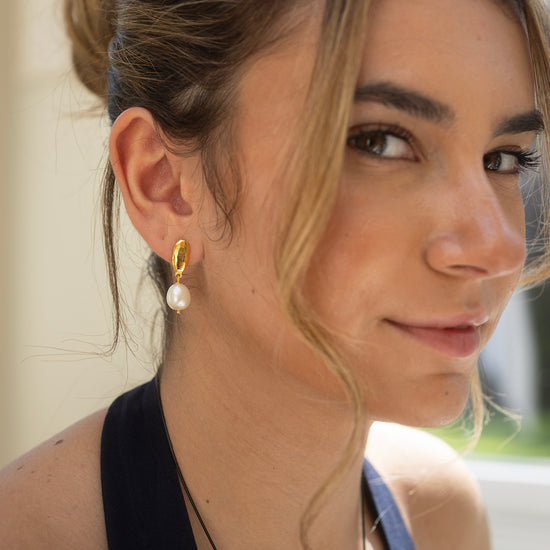 Close-up of a woman wearing gold earrings with pearls, outdoors.