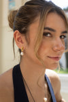 Close-up of a woman wearing gold earrings with pearls, outdoors.