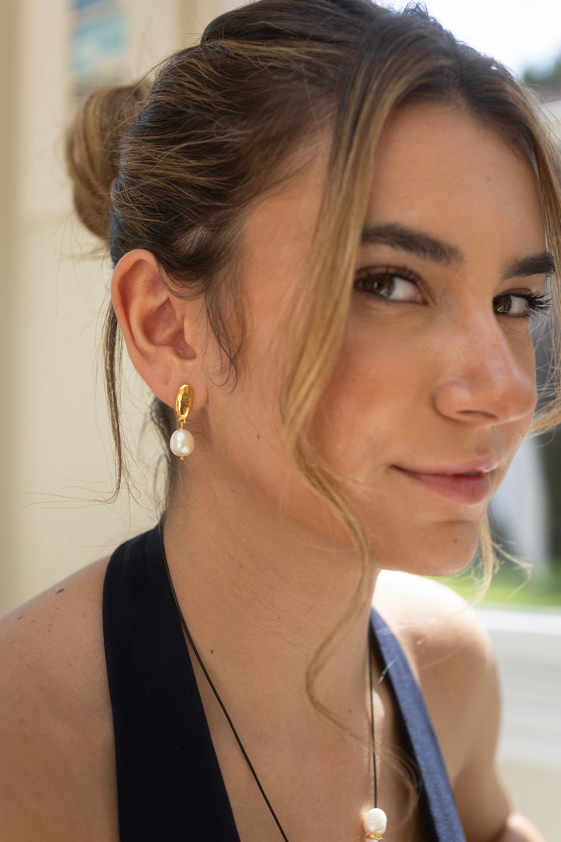 Close-up of a woman wearing gold earrings with pearls, outdoors.