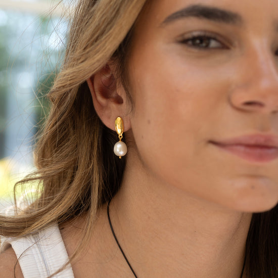 Close-up of a woman wearing a pearl earring with a blurred outdoor background
