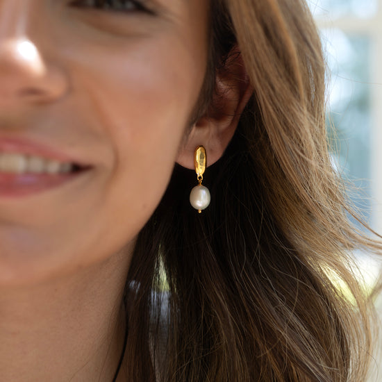Close-up of a woman wearing a pearl earring with a blurred outdoor background