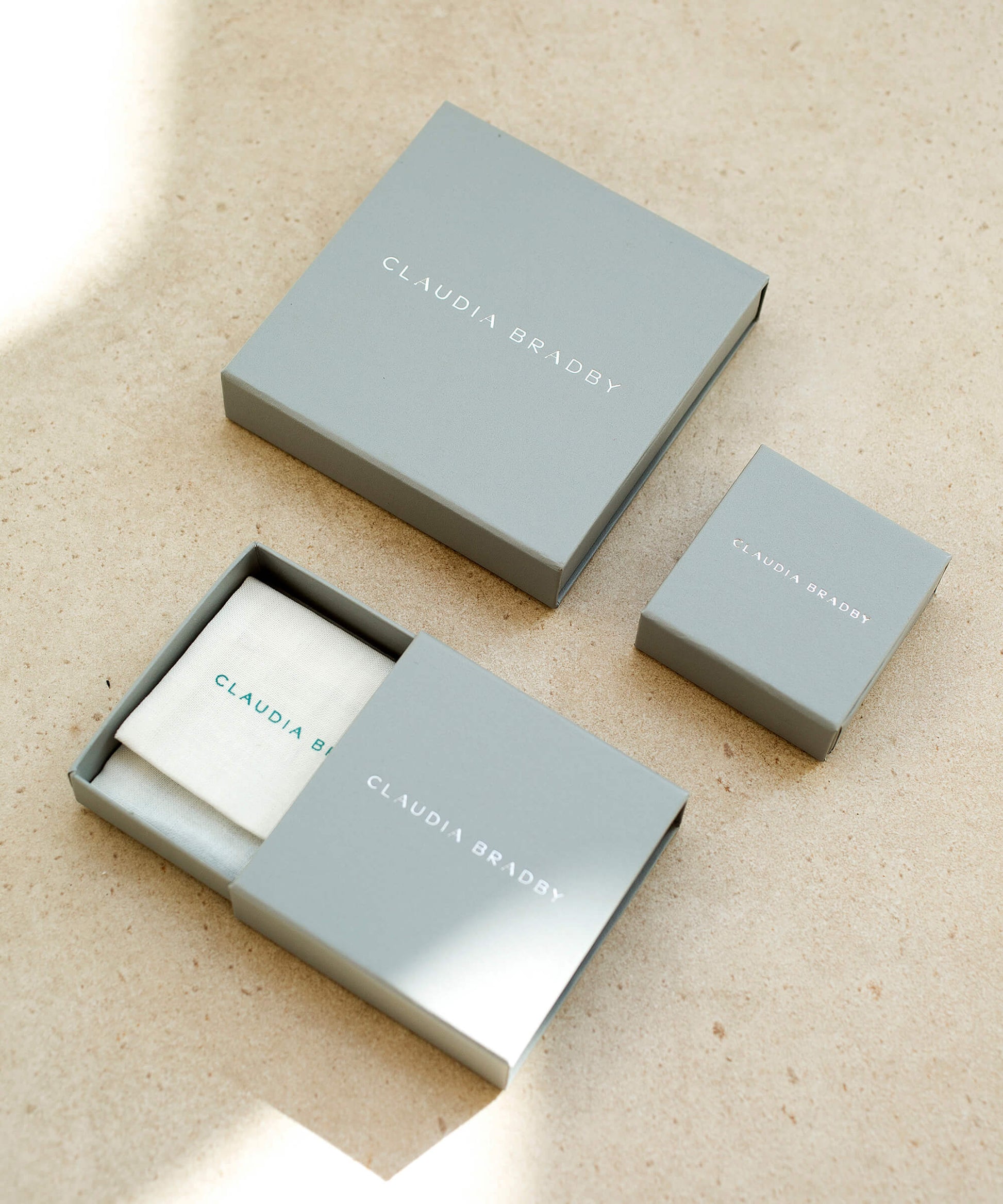 Three gray boxes with 'Claudia Bradby' branding on a beige surface