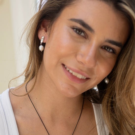 Woman wearing pearl earrings by Claudia Bradby and a necklace with a neutral background 