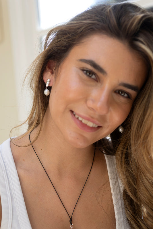 Woman wearing pearl earrings by Claudia Bradby and a necklace with a neutral background 