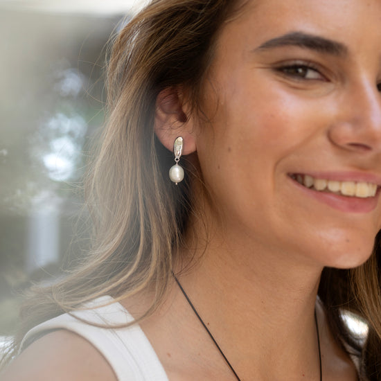 Woman wearing pearl earrings by Claudia Bradby with a blurred natural background