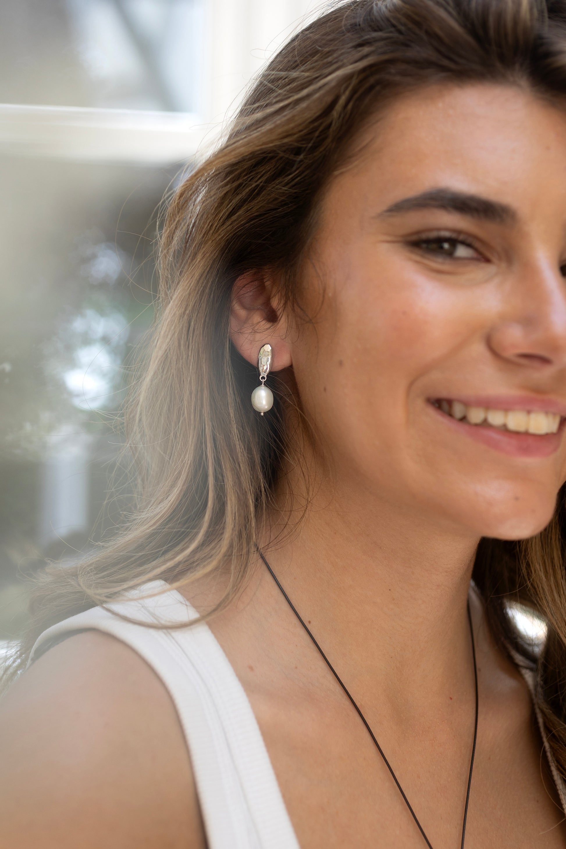 Woman wearing pearl earrings by Claudia Bradby with a blurred natural background