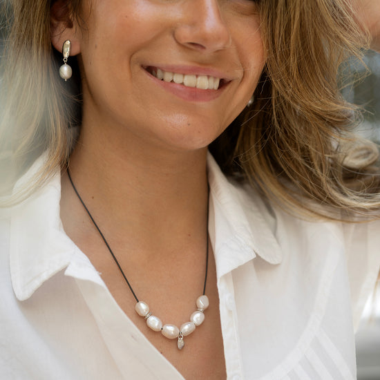 Woman wearing a pearl necklace and earrings, smiling outdoors.