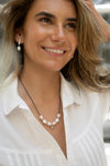 Woman wearing a pearl necklace and earrings, smiling outdoors.