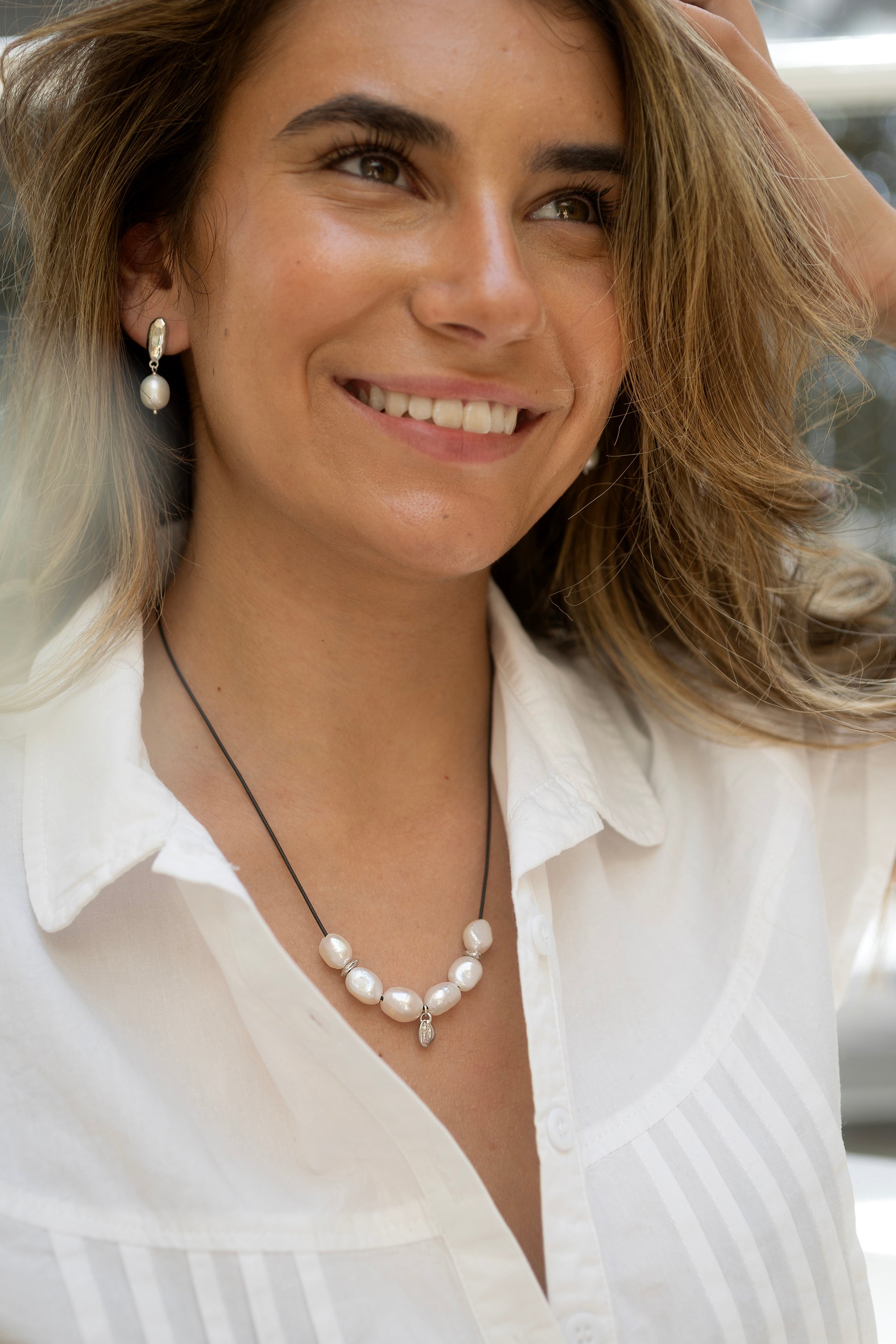 Woman wearing a pearl necklace and earrings, smiling outdoors.