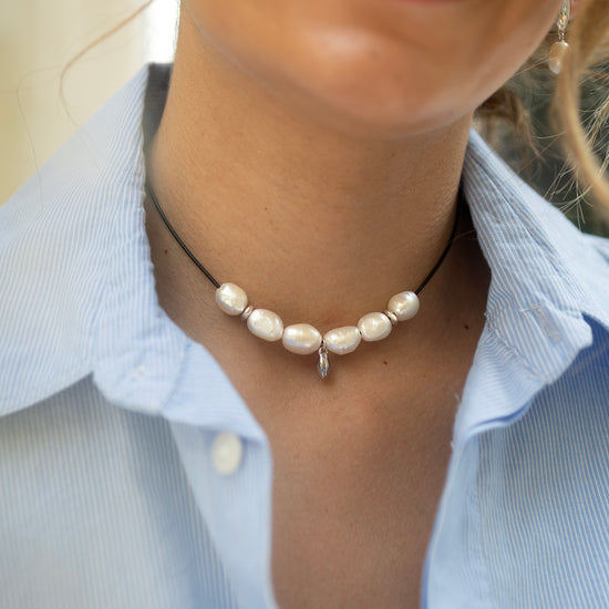 Close-up of a person wearing a pearl necklace with a light blue shirt.