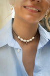 Close-up of a person wearing a pearl necklace with a light blue shirt.