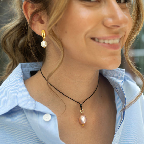 Woman wearing a necklace with a pink pearl pendant and pearl earrings.