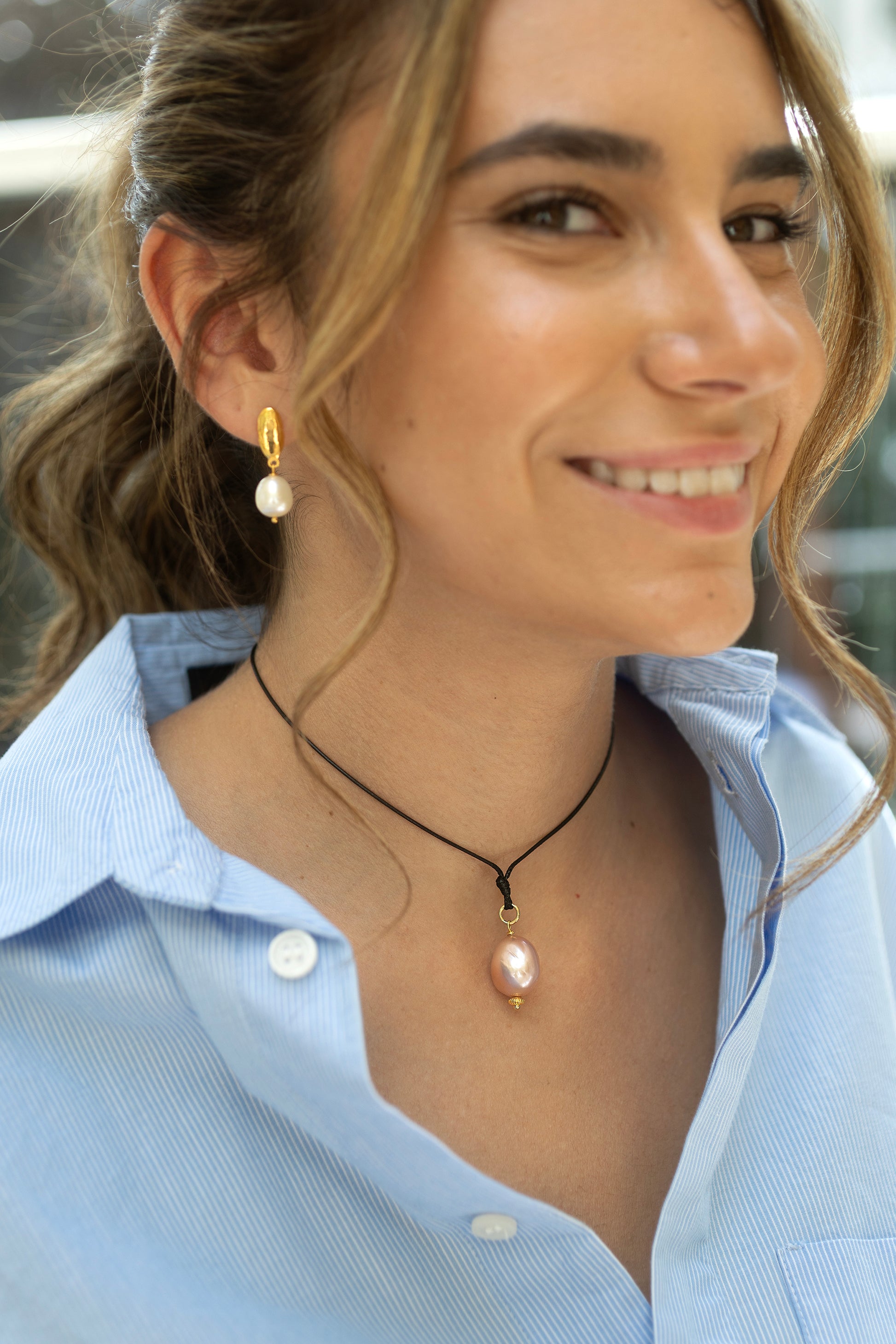 Woman wearing a necklace with a pink pearl pendant and pearl earrings.