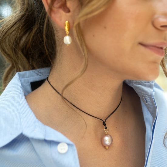Close-up of a woman wearing pearl earrings and a necklace with a pink pendant.