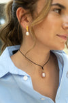 Close-up of a woman wearing pearl earrings and a necklace with a pink pendant.