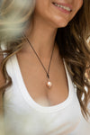 Woman wearing a necklace with a pink pendant, blurred background