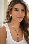 Woman wearing a white tank top and pearl necklace with earrings, outdoors.