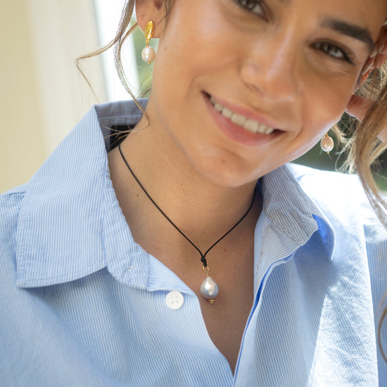 Woman wearing a light blue shirt with a pearl necklace and earrings.