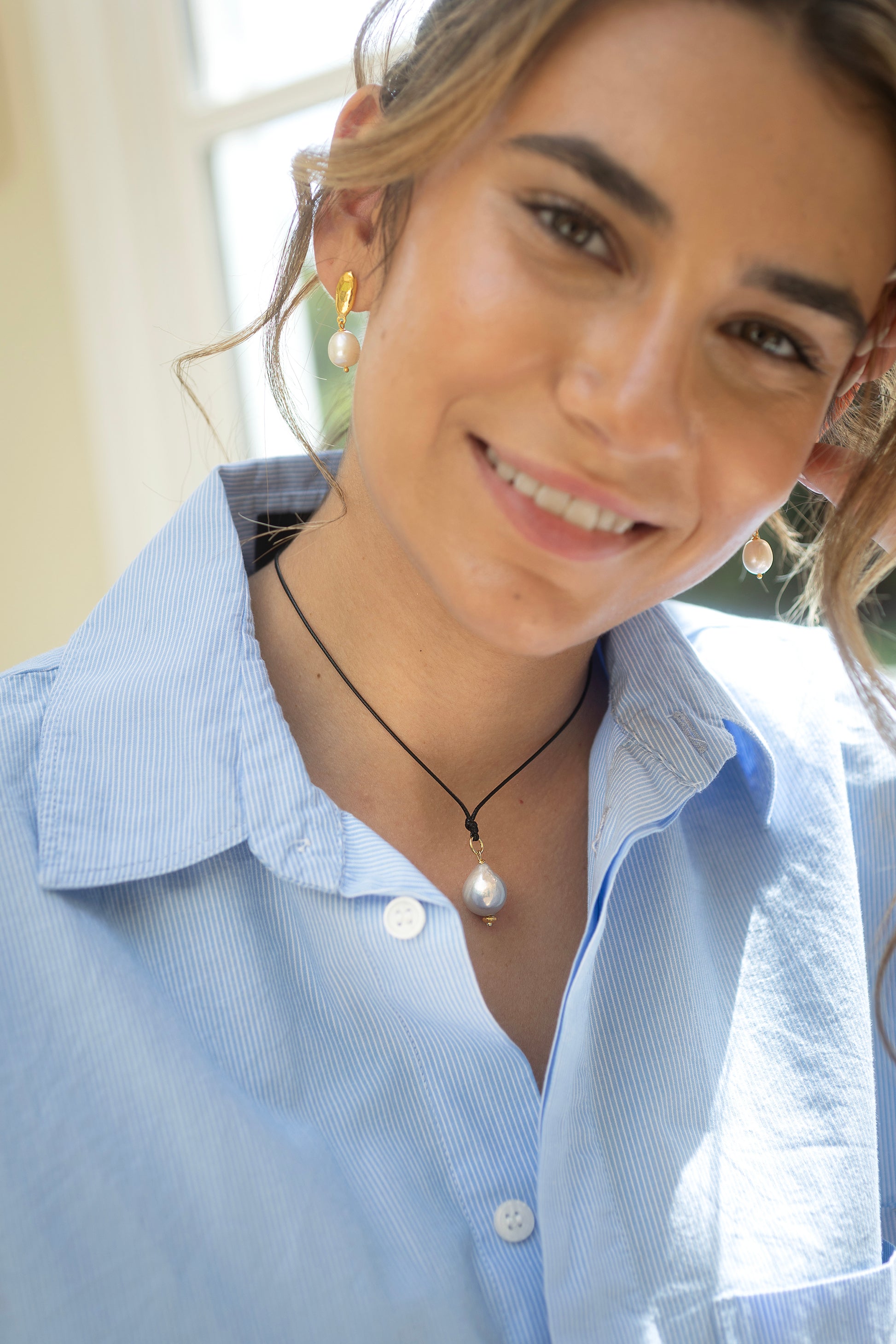 Woman wearing a light blue shirt with a pearl necklace and earrings.