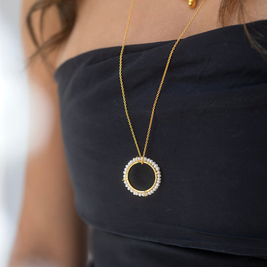 Close-up of a person wearing a gold necklace with a circular pendant on a blurred background