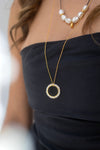 Close-up of a person wearing a gold necklace with a circular pendant on a blurred background