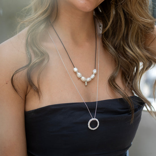 Woman wearing a black strapless top and pearl necklace with a blurred background