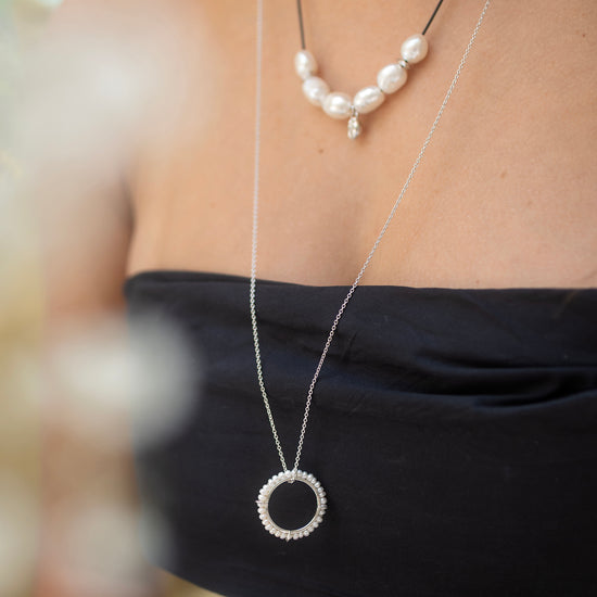 Close-up of a person wearing two necklaces with pearls and a circular pendant.