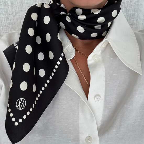 Person wearing a black polka dot scarf on a white shirt against a light gray background