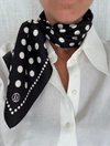 Person wearing a black polka dot scarf on a white shirt against a light gray background