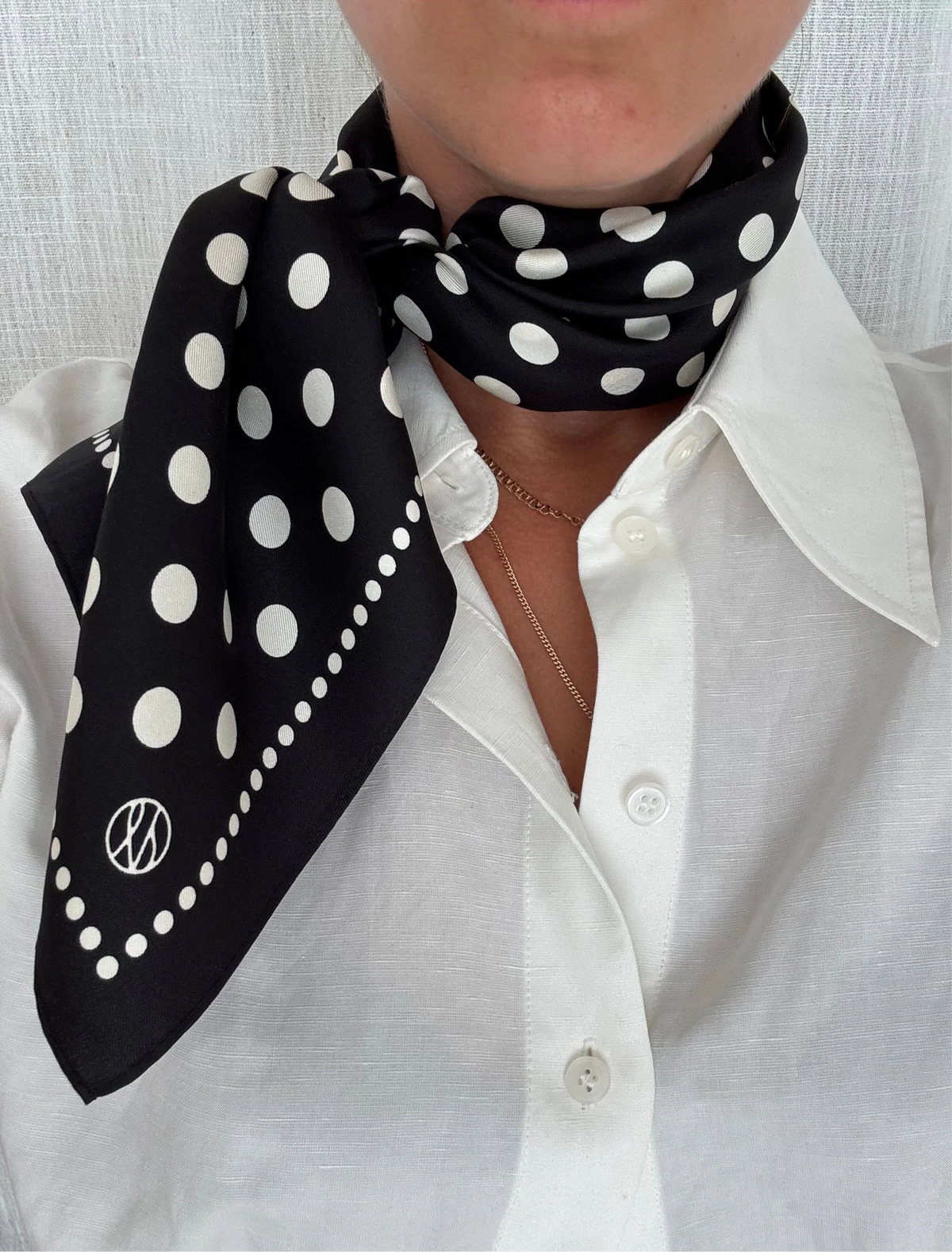 Person wearing a black polka dot scarf on a white shirt against a light gray background