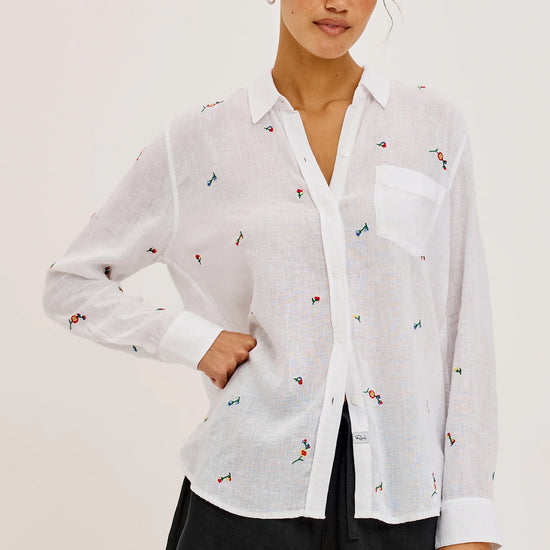 Woman wearing a white blouse with small colorful patterns and black shorts on a light background
