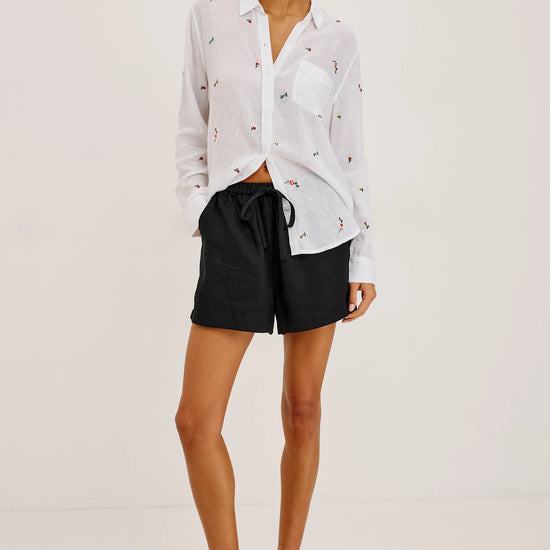 Woman wearing a white blouse with black patterns and black shorts on a light gray background