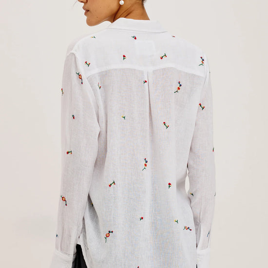 Woman wearing a white blouse with small colorful patterns on a plain background
