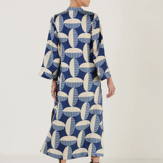 Woman wearing a blue and white patterned kaftan dress from Mondo Corsini on a white background. Rear view