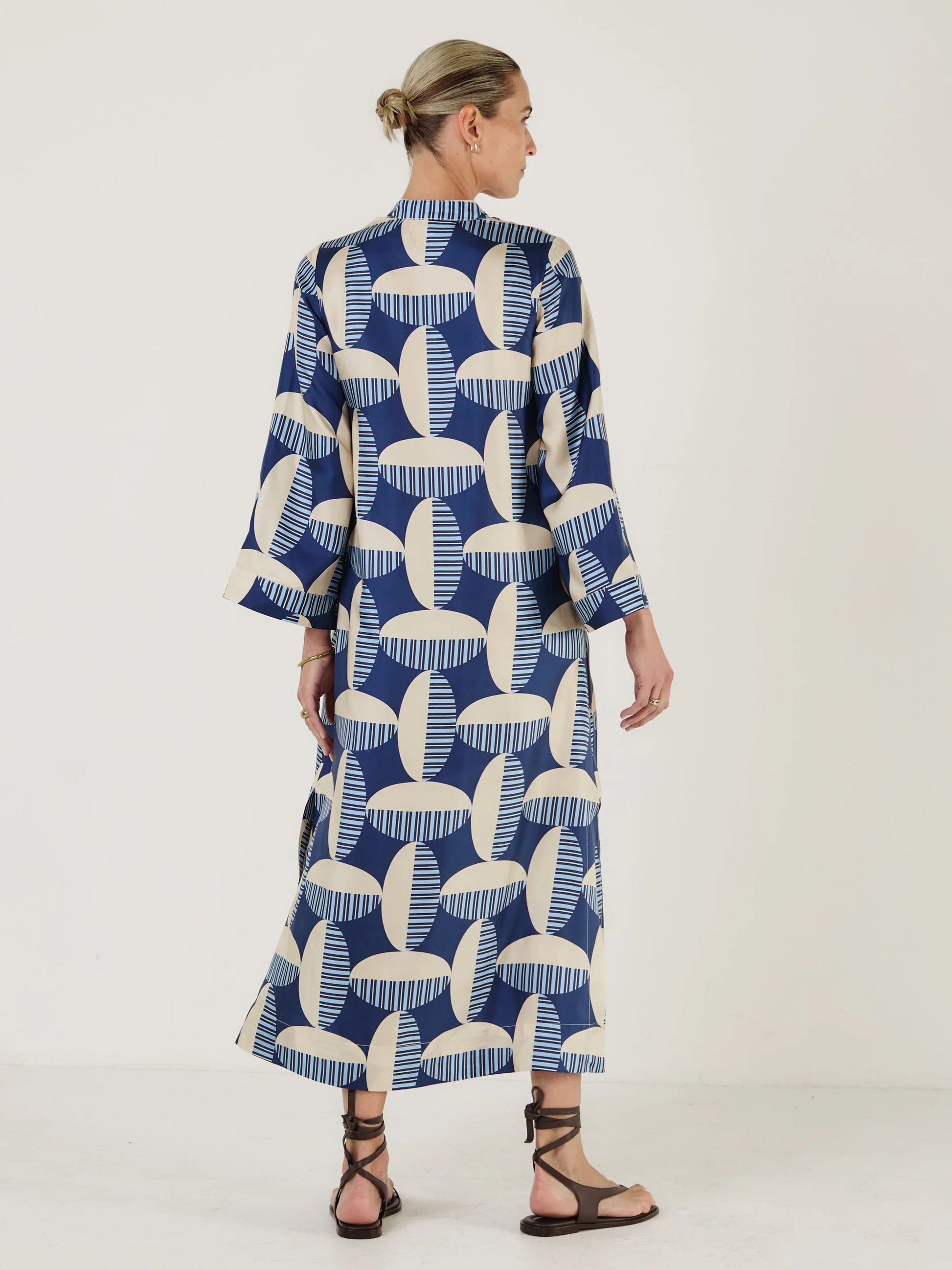Woman wearing a blue and white patterned kaftan dress from Mondo Corsini on a white background. Rear view