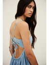 Woman wearing a light blue denim dress with thin straps and open back against a plain background