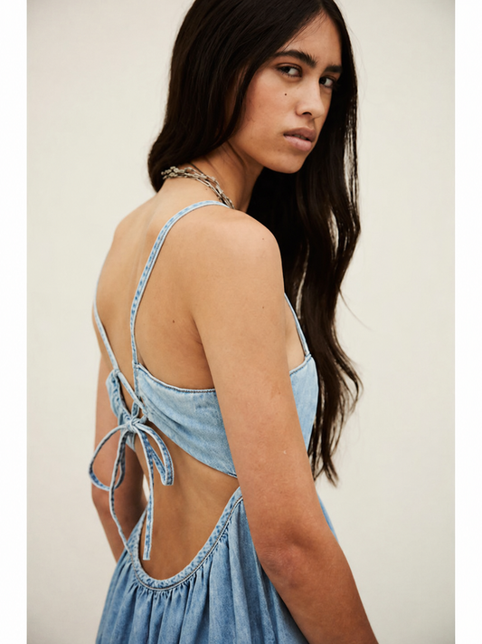 Woman wearing a light blue denim dress with thin straps and open back against a plain background