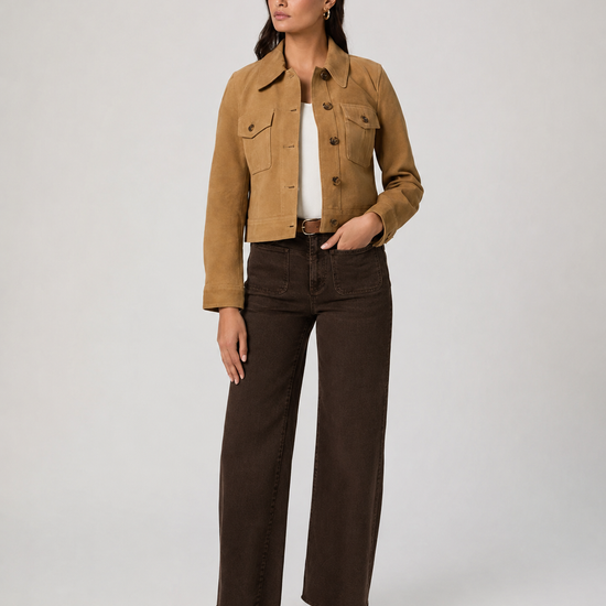 A woman modeling a cropped tan suede jacket over a white top, paired with dark brown wide-leg jeans and tan suede loafers, against a light gray studio background.