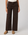 A model wearing dark brown wide-leg denim jeans with a frayed hem and tan suede slip-on shoes, shown from the waist down on a light gray studio background.