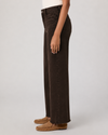 A side-profile view of a model wearing dark brown wide-leg denim jeans and tan suede moccasin loafers against a light gray studio background.
