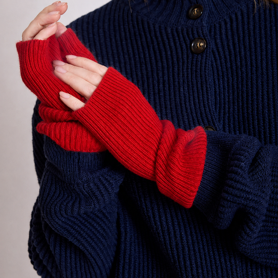 A close-up of a person wearing a navy blue ribbed knit sweater with red fingerless knit sleeves, showing the hands and upper torso against a plain light background.