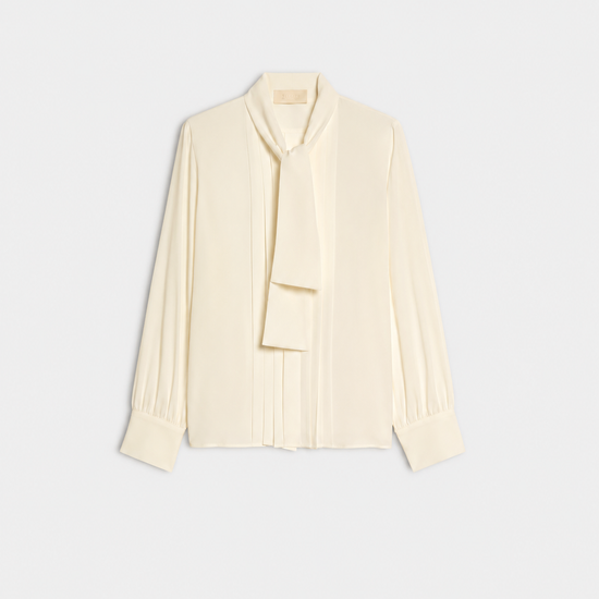 A cream long-sleeve blouse with a draped tie-neck detail, shown flat against a light gray background.