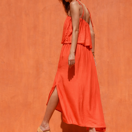 Woman in a bright orange dress standing against an orange wall