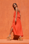 Woman in a bright orange dress standing against an orange wall